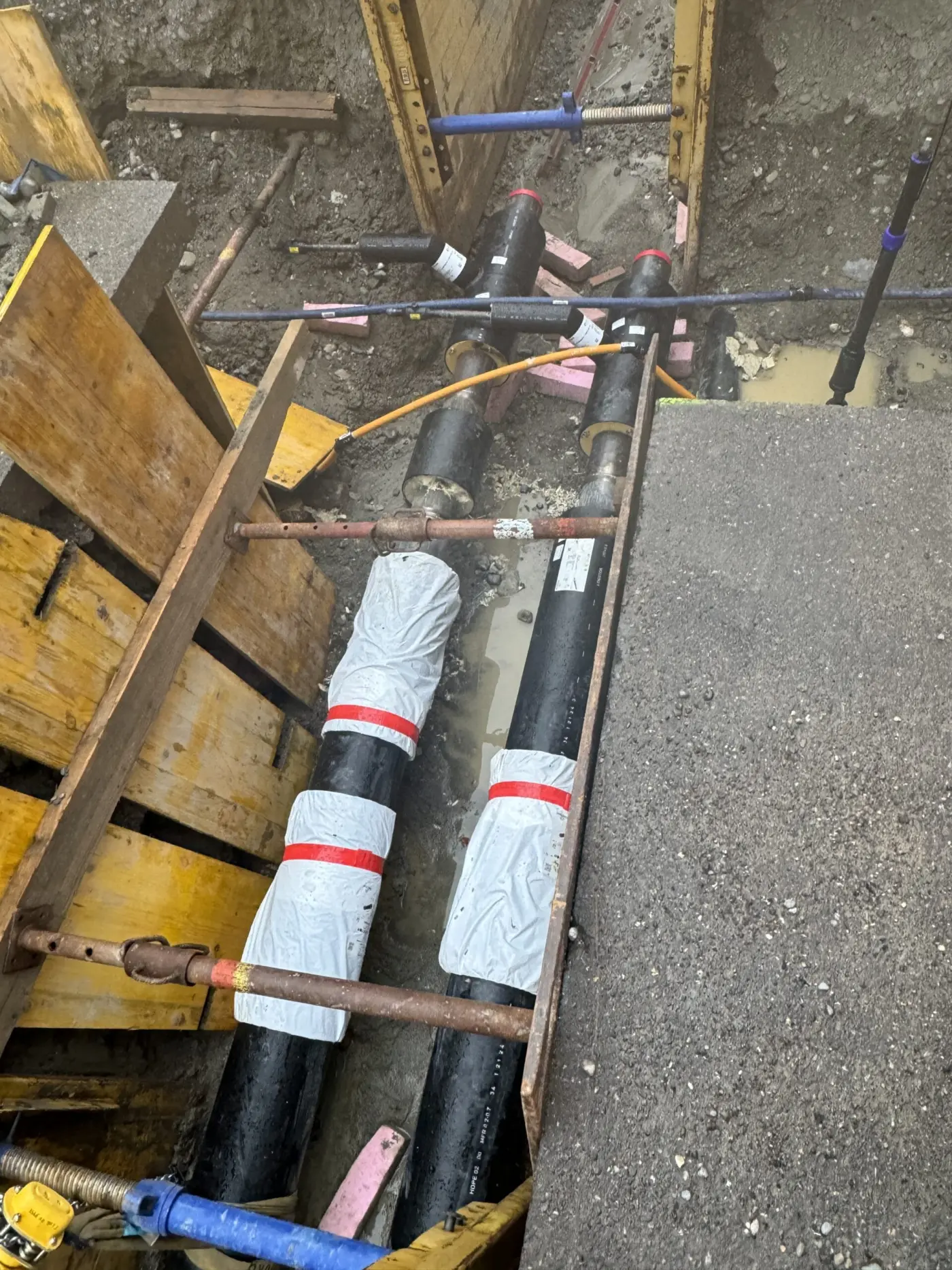 Fernwärmeleitungen in innerstädtischer Baugrube mit Verbauboxen und vorbereiteten Muffen, die Verfüllung mit Flüssigboden erfolgt grabenfüllend und erschütterungsarm