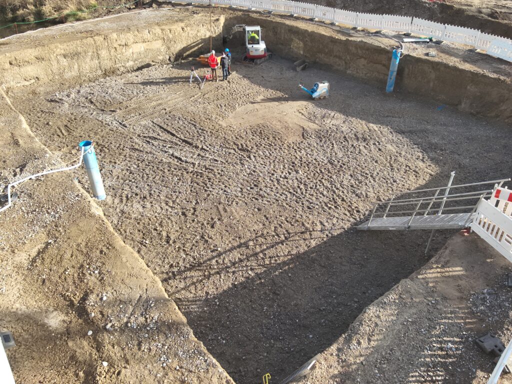 Übersicht der Baugrube, in der hinteren Ecke steht ein Mann in oranger Arbeitsbekleidung