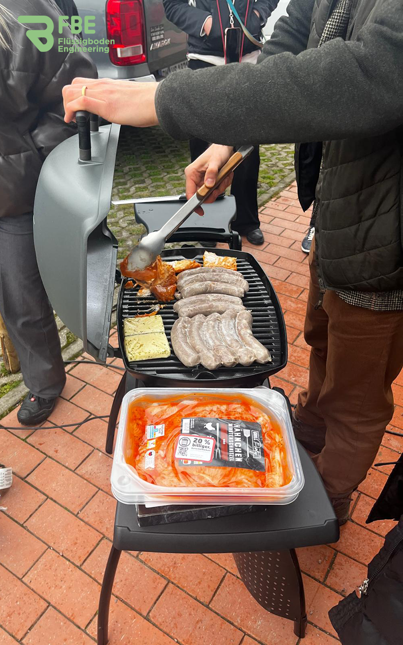 Vollbelegter Grill mit einer Person davor, die eine Zange in der Hand hält und grillt