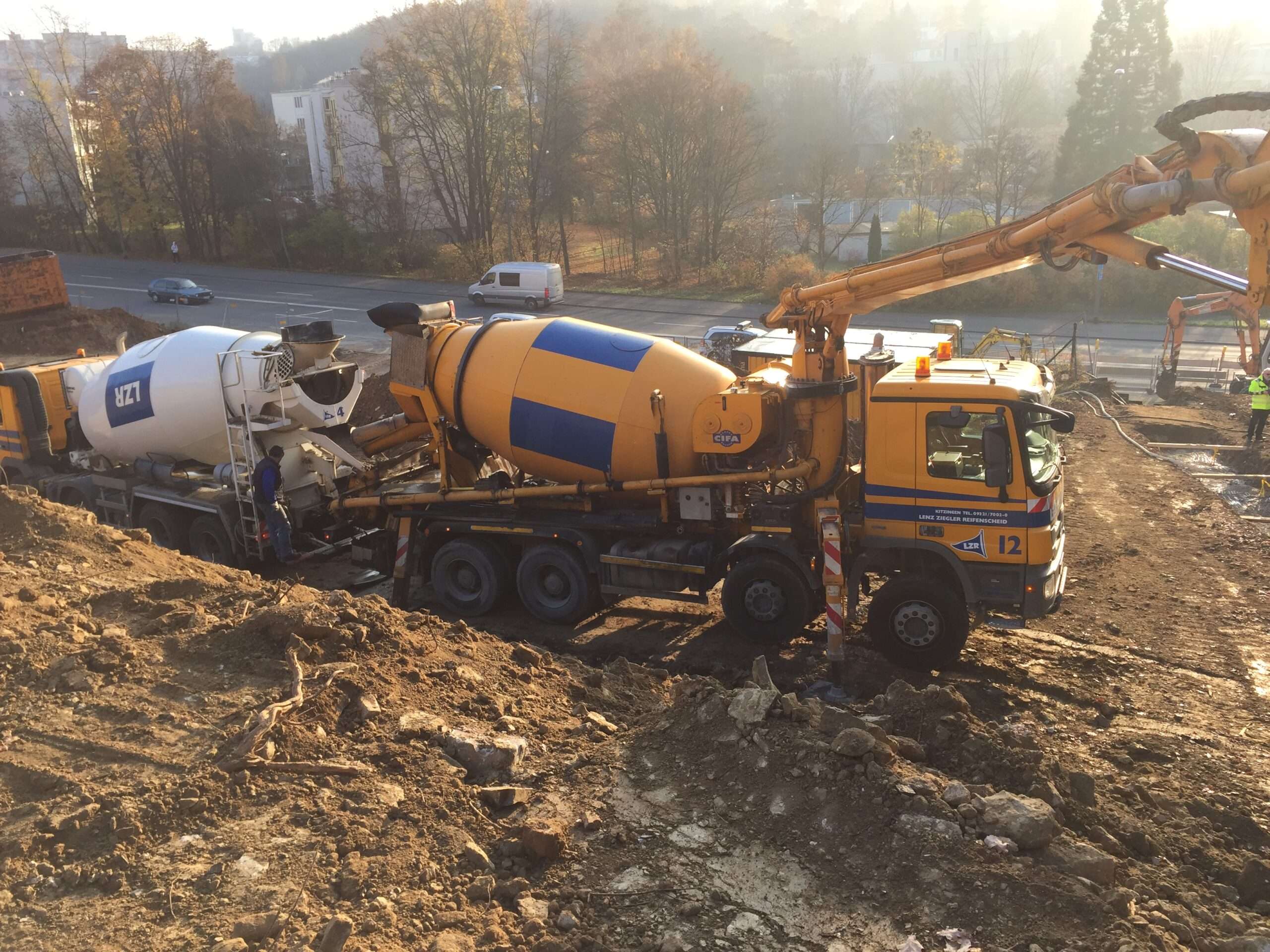 Betonpumpe am Hangfuß aufgestellt - Fahrmischer aus dem Mischwerk übergibt Flüssigboden an die Pumpe